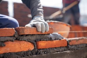 bricklayer-industrial-worker-installing-brick-masonry-with-trowel-putty-knife-construction-site